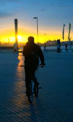 Silhouette man riding bicycle on street against sky during sunset