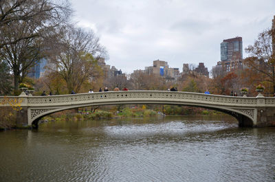 Arch bridge over river by buildings against sky