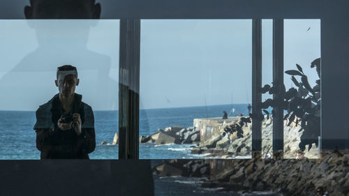 Man standing by sea against sky seen through window