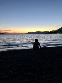 Silhouette men sitting on beach against sky during sunset