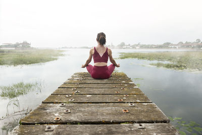 Young woman sitting on pier over lake