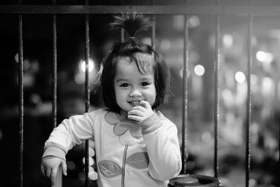 Portrait of cute smiling girl with finger in mouth against fence