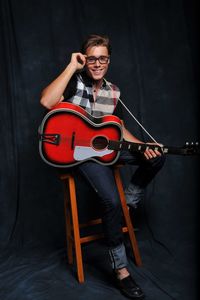 Smiling young man with guitar sitting on stool