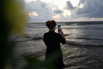 Rear view of woman standing at beach against sky during sunset