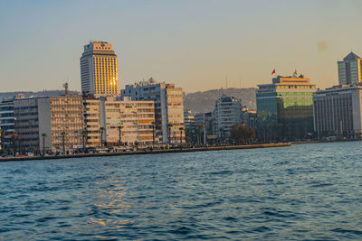 Modern buildings by river against sky in city