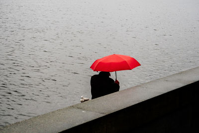 High angle view of man with red umbrella by retaining wall against lake