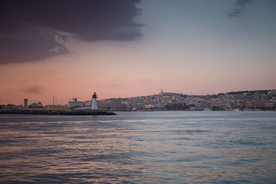 Sea and buildings against sky at sunset