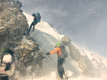 Low angle view of men climbing on snowcapped rocky mountain