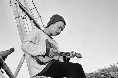 Low angle view of man sitting on guitar against clear sky