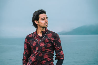 Young man looking at sea against sky