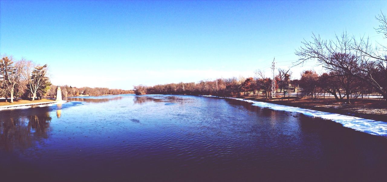 clear sky, water, blue, tree, copy space, waterfront, winter, cold temperature, snow, nature, tranquil scene, tranquility, river, beauty in nature, scenics, lake, season, bare tree, built structure, building exterior