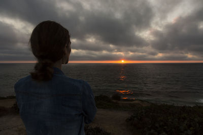 Rear view of woman looking at sea shore against sunset sky