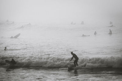 People surfboarding in sea during foggy weather