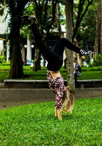 Young woman doing handstand on grassy field at park