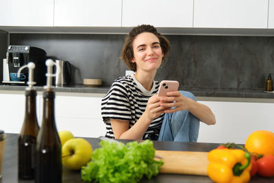 Portrait of smiling young woman using mobile phone in kitchen