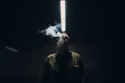 Man smoking while standing in darkroom