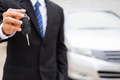 Midsection of salesman holding key while standing against car