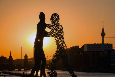 Silhouette people against buildings in city during sunset