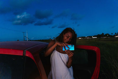 Portrait of a young woman taking photos with a mobile phone of a sunset on a road in bahia