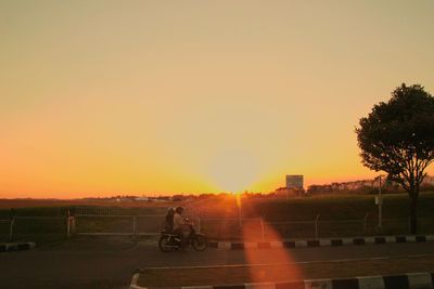 Man riding bicycle on road against sky during sunset