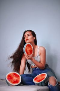 Young woman looking away while sitting with watermelons around