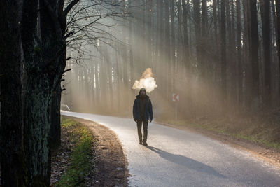 Man walking on road amidst bare trees in forest