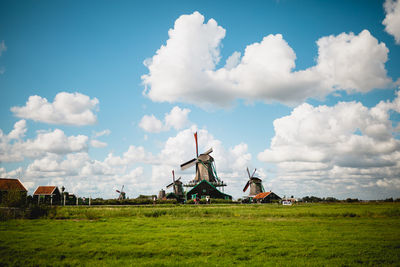 Traditional windmill on field against sky with fluffy clouds