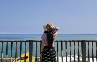 Rear view of woman wearing hat standing by sea against clear sky