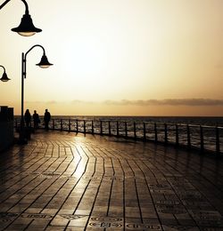 Street lights on footpath by sea against clear sky