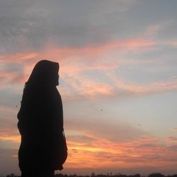 Silhouette woman standing against orange sky