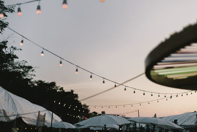 Low angle view of lighting equipment hanging against sky at sunset