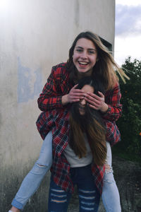 Young woman piggybacking friend while standing by wall