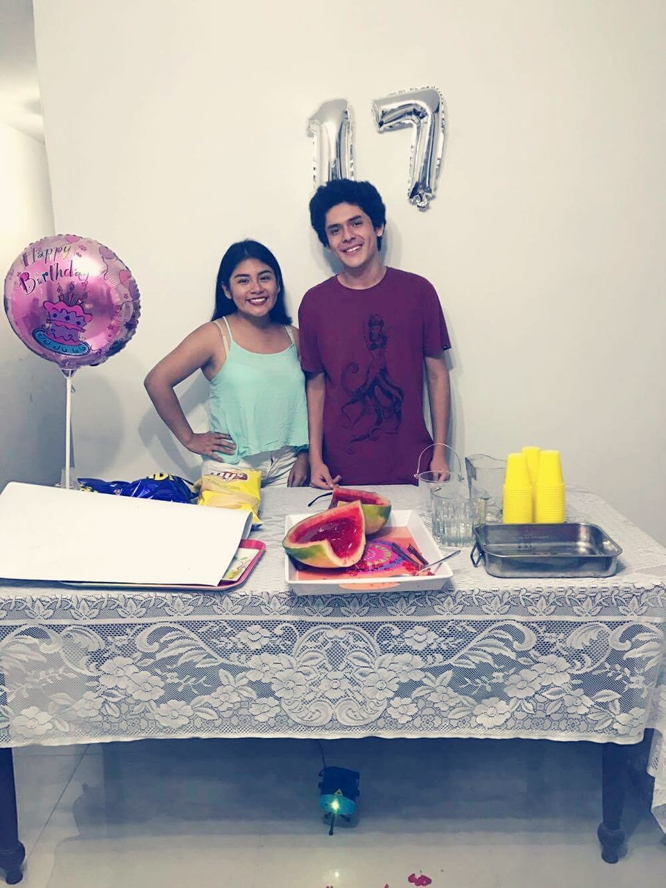 front view, young adult, looking at camera, young women, portrait, balloon, young men, happiness, real people, smiling, standing, indoors, two people, table, celebration, food and drink, togetherness, holding, birthday cake, sitting, lifestyles, friendship, wineglass, day