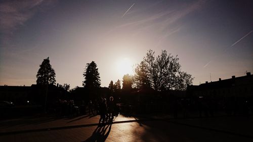 Silhouette trees by street against sky during sunset