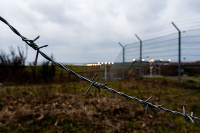 Barbed wire fence on field against sky