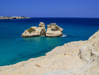 Rocks in sea against clear blue sky