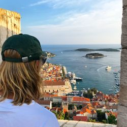 Woman looking at view of cityscape by sea against sky