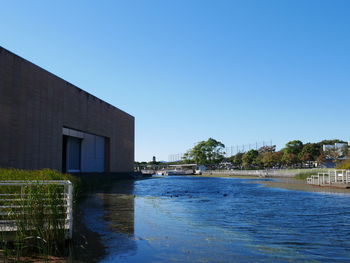 Buildings by lake against clear blue sky