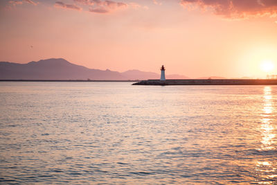Silhouette lighthouse by sea against sky during sunset