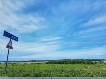 Road sign on field against sky