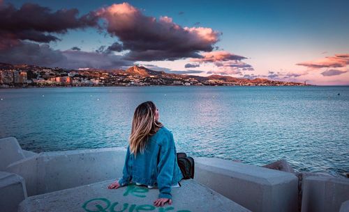 Rear view of woman sitting on seat against sea during sunset