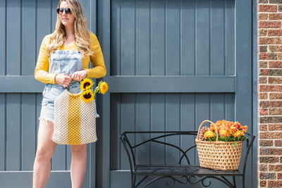 Woman holding yellow flowers in purse against wall