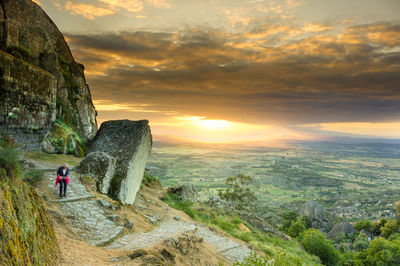 Man standing on cliff by sea against sky during sunset