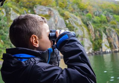 Side view of boy looking at lake through binoculars