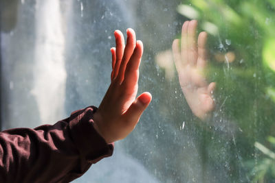 Cropped image of hand holding wet glass during rainy season