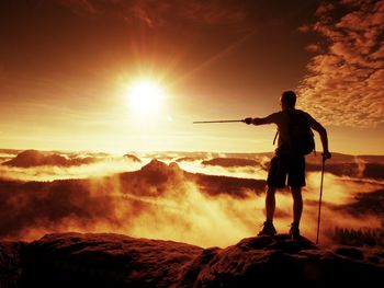 Tourist with sporty backpack and poles in hands stand on summit and watch into  misty valley bellow