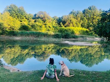 Rear view of woman with dog sitting at lakeshore