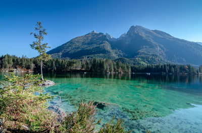 Scenic view of lake and mountains against clear blue sky