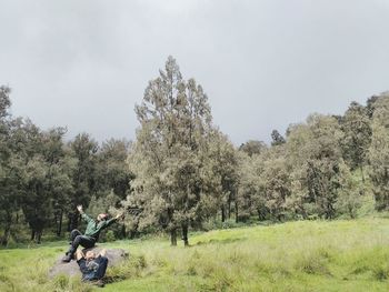 People sitting on field by trees against sky