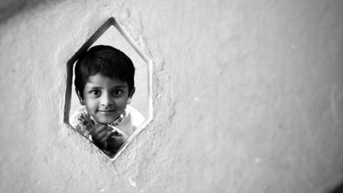 Portrait of cute boy peeking through window on wall